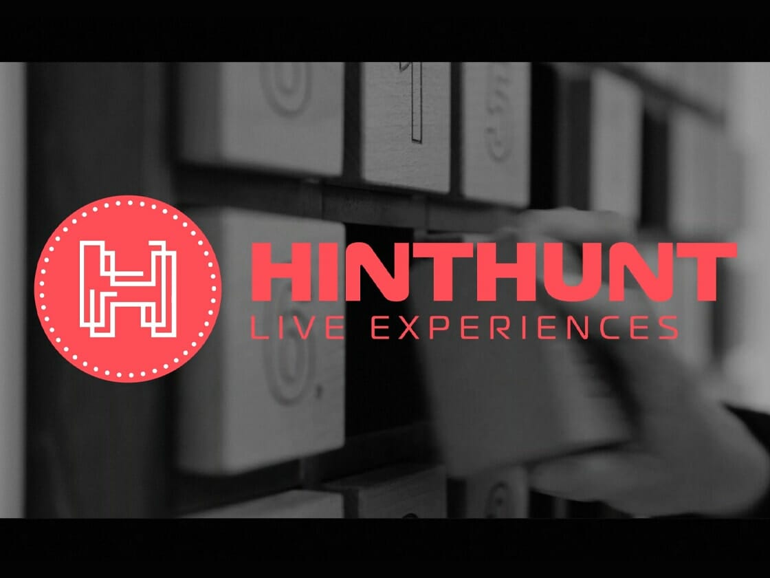 A hand interacts with puzzle elements next to the hinthunt live experiences logo, suggesting an escape room or puzzle game activity.