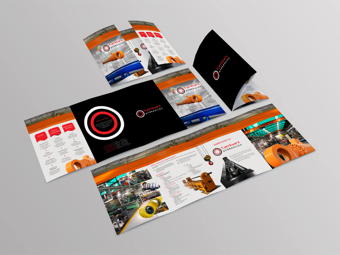 Project Tambani Hydraulics A set of opened and closed tri-fold brochures displayed on a light gray surface. The brochures feature a black, white, orange, and red color scheme, industrial imagery, product photos, and circular graphic elements, with technical content and a modern, professional layout.